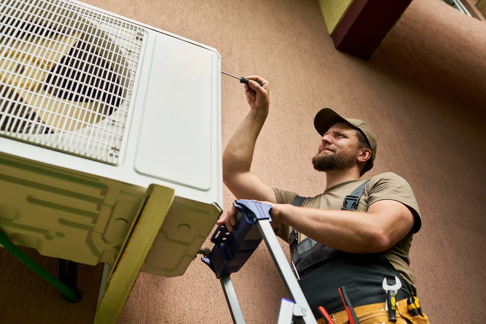 HVAC technician on a ladder servicing an outdoor mini-split air conditioning unit
